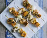 Spiedini di pesce misti, con gamberi, calamari e salmone, conditi con erbe aromatiche e serviti su un piatto bianco.