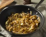 Cipolle caramellate in padella, pronte per insaporire un piatto. Un cucchiaio di legno attende accanto.