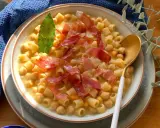 Un piatto fumante di pasta e ceci, guarnito con prosciutto crudo e una foglia di alloro.