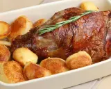 Un succulento agnello al forno con patate arrosto dorate, guarnito con un rametto di rosmarino fresco.