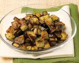 Melanzane a funghetto dorate e saporite, condite con erbe aromatiche, servite in una ciotola di vetro.