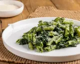 Piatto di pasta con spinaci e parmigiano grattugiato, servito su un piatto bianco.
