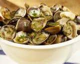 Un invitante sautè di vongole, condito con prezzemolo fresco e olio d'oliva, servito in una ciotola bianca su un tavolo di legno.