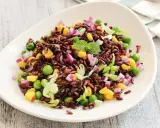 Insalata di riso Venere colorata con piselli, mais, cipolla rossa e lattuga croccante, guarnita con menta fresca.