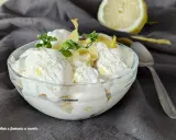 Coppa di cremoso gelato al limone, guarnita con scorzette e foglioline di menta. Un limone fresco sullo sfondo.