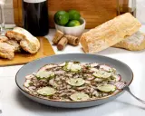 Delizioso carpaccio di polpo, guarnito con fette di lime e erbe aromatiche, pronto per essere gustato con pane fresco e vino.