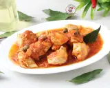 Succulento pollo alla pizzaiola in un piatto bianco, con capperi, pomodoro e foglie di alloro. Accanto, peperoncini secchi e una bottiglia d'olio.