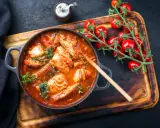 Un invitante guazzetto di pesce in umido, con pomodorini freschi e erbe aromatiche, pronto per essere gustato.