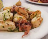 Calamari in padella, succulenti e dorati, conditi con prezzemolo fresco e serviti con una fetta di limone.