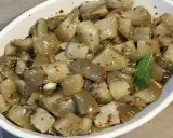 Un invitante piatto di insalata di melanzane, condita con olio, aglio e peperoncino, guarnita con una fogliolina di menta.