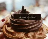 Una mano con smalto rosso tiene un delizioso dolce al cioccolato, decorato con la scritta "cioccolatitaliani".