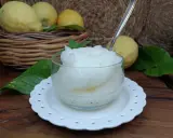 Granita al limone fatta in casa, fresca e dissetante, servita in una coppetta con foglioline di menta. Limoni freschi in un cesto sullo sfondo.