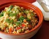 Tabulè di verdure fresco e colorato, con pomodori, zucchine e erbe aromatiche, servito in una ciotola di terracotta.