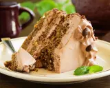 Una fetta di torta al cioccolato con abbondante crema al latte, guarnita con chicchi di caffè e una fogliolina di menta.