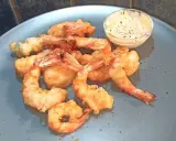 Gamberi in tempura dorati e croccanti, serviti su un piatto blu con una ciotolina di salsa cremosa.