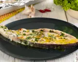 Un succulento pesce spada al forno, condito con erbe aromatiche e olio d'oliva, servito su un piatto scuro.