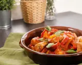 Un saporito spezzatino di vitello con peperoni rossi e gialli, guarnito con foglie di salvia fresca, servito in una ciotola di terracotta.