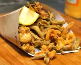 Un cono di carta marrone traboccante di una deliziosa frittura di pesce croccante, con calamari, gamberetti e pesciolini, guarnito con uno spicchio di limone.