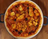 Un saporito baccalà in umido con patate e olive nere, guarnito con prezzemolo fresco, in una casseruola su un tavolo di legno.