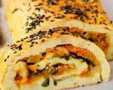 Rotolo di patate dorato, cosparso di semi neri, con un ripieno colorato di verdure.