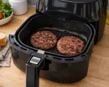 Due hamburger succulenti cuociono nella friggitrice ad aria, pronti per essere serviti con pane tostato e pomodorini.