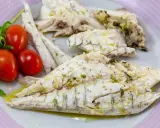 Filetti di branzino in padella, conditi con erbe aromatiche e olio d'oliva, serviti con pomodorini e rucola.