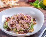 Insalata di ceci e tonno con olive nere e cipolla rossa, servita in un piatto bianco su un tavolo di legno.