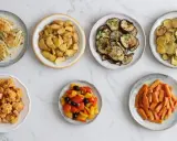 Sette piatti di verdure in friggitrice ad aria: finocchi, patate, melanzane, zucchine, cavolfiore, peperoni e carote.