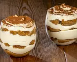 Due bicchieri di delizioso tiramisù senza uova, con strati di crema e savoiardi, spolverati di cacao.