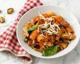 Piatto di pasta alla norma con melanzane fritte, pomodoro, basilico e ricotta salata grattugiata.