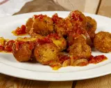 Polpette di pesce dorate e saporite, condite con un sugo rosso di pomodoro e cipolla, servite su un piatto bianco.