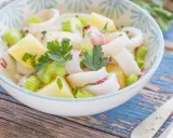 Insalata di calamari fresca con patate, sedano e prezzemolo, servita in una ciotola decorata su un tavolo di legno blu.