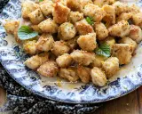 Bocconcini di pollo dorati e croccanti, guarniti con scorza di limone e foglioline di menta, serviti su un piatto decorato.
