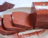 Fette di budino al cioccolato, spolverate di cacao e cocco, su un piatto.