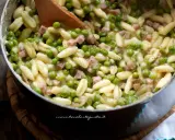 Un primo piatto invitante: pasta e piselli cremosa con cubetti di prosciutto cotto, mescolata con un cucchiaio di legno.