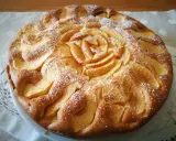 Deliziosa torta di mele senza glutine, decorata con fettine di mela disposte a rosa al centro e petali tutt'intorno, spolverata di zucchero a velo.