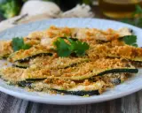 Fette di zucchine al forno, impanate e dorate, guarnite con prezzemolo fresco. Un contorno leggero e gustoso.