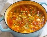 Un fumante minestrone di verdure in una pentola azzurra, ricco di carote, zucchine, piselli e cavolfiore.