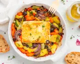 Feta al forno con verdure miste, olive nere e erbe aromatiche, accompagnata da pane rustico e olio d'oliva.