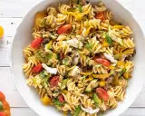 Un piatto invitante di pasta fredda saporita con fusilli, pomodorini, zucchine, peperoni gialli e mozzarella.