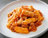Piatto di rigatoni conditi con un ricco ragù, spolverati di parmigiano. La pasta alla zozzona ricetta perfetta per un pranzo gustoso.