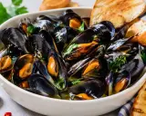Soute di cozze fumante in una ciotola bianca, guarnita con prezzemolo fresco e accompagnata da fette di pane tostato.