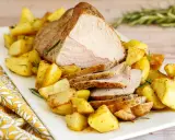 Un succulento arrosto di vitello affettato, servito su un piatto bianco con patate arrosto dorate e rametti di rosmarino.