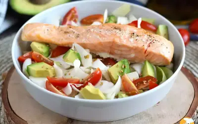 Salmone cotto su un letto di avocado, pomodorini e cipolla bianca, un piatto leggero e gustoso, perfetto come secondi di pesce.