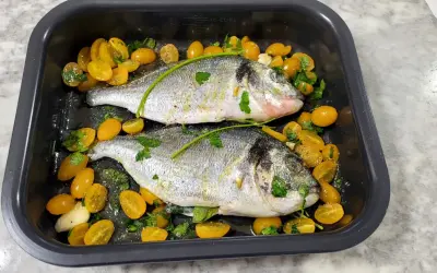 Due orate pronte per la friggitrice ad aria, condite con pomodorini gialli, aglio e prezzemolo.