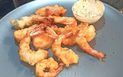 Gamberi in tempura dorati e croccanti, serviti su un piatto blu con una ciotolina di salsa cremosa.