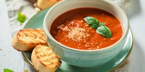 Una ciotola di cremosa zuppa di pomodoro, guarnita con basilico fresco e parmigiano, servita con crostini tostati.