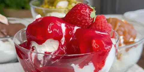 Coppetta di gelato alla fragola, con fragole fresche e salsa rossa. Scopri come fare il gelato senza gelatiera per un dessert delizioso.