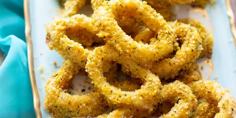 Anelli di totano al forno dorati e croccanti, serviti su un piatto azzurro con un tovagliolo turchese.