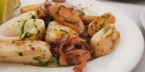 Calamari in padella, succulenti e dorati, conditi con prezzemolo fresco e serviti con una fetta di limone.